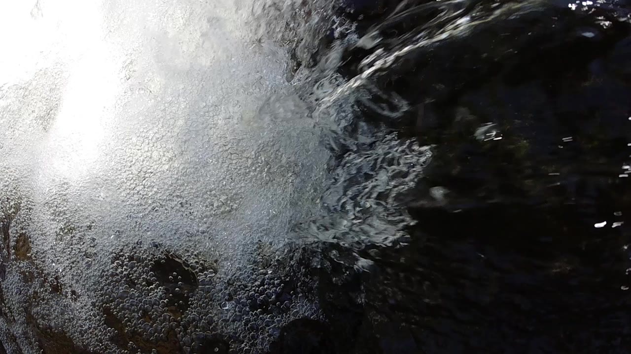 High-angle close-up of white churning foam from a waterfall striking dark water in Colorado; no people visible