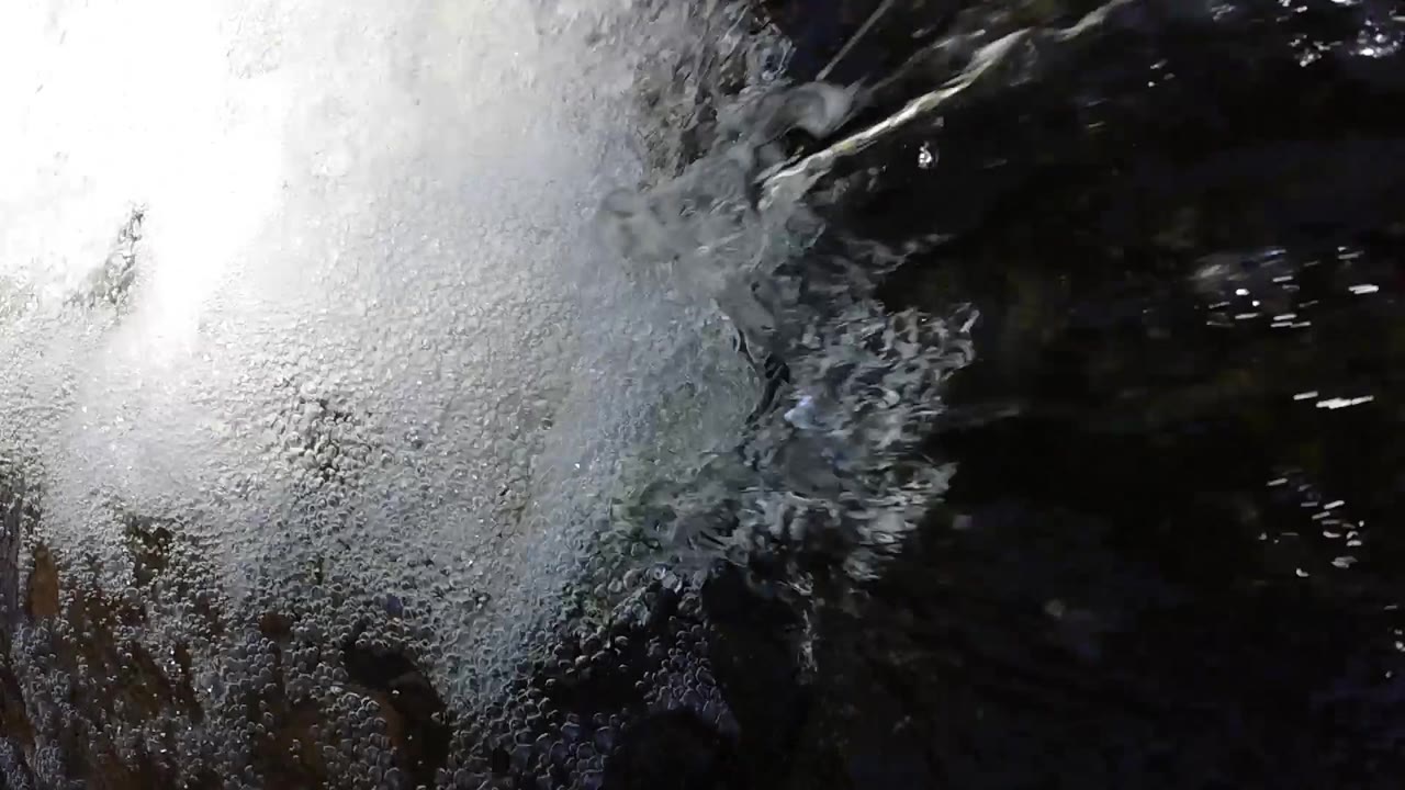High-angle close-up aerial view of white foam and a visible water stream falling into a dark pool in Colorado; no people visible