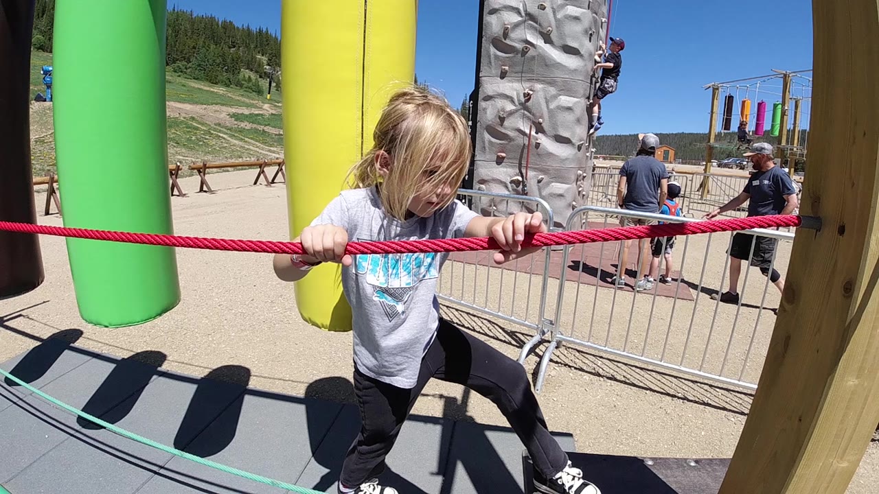 Girl leans forward while holding the red rope near yellow and green obstacles.