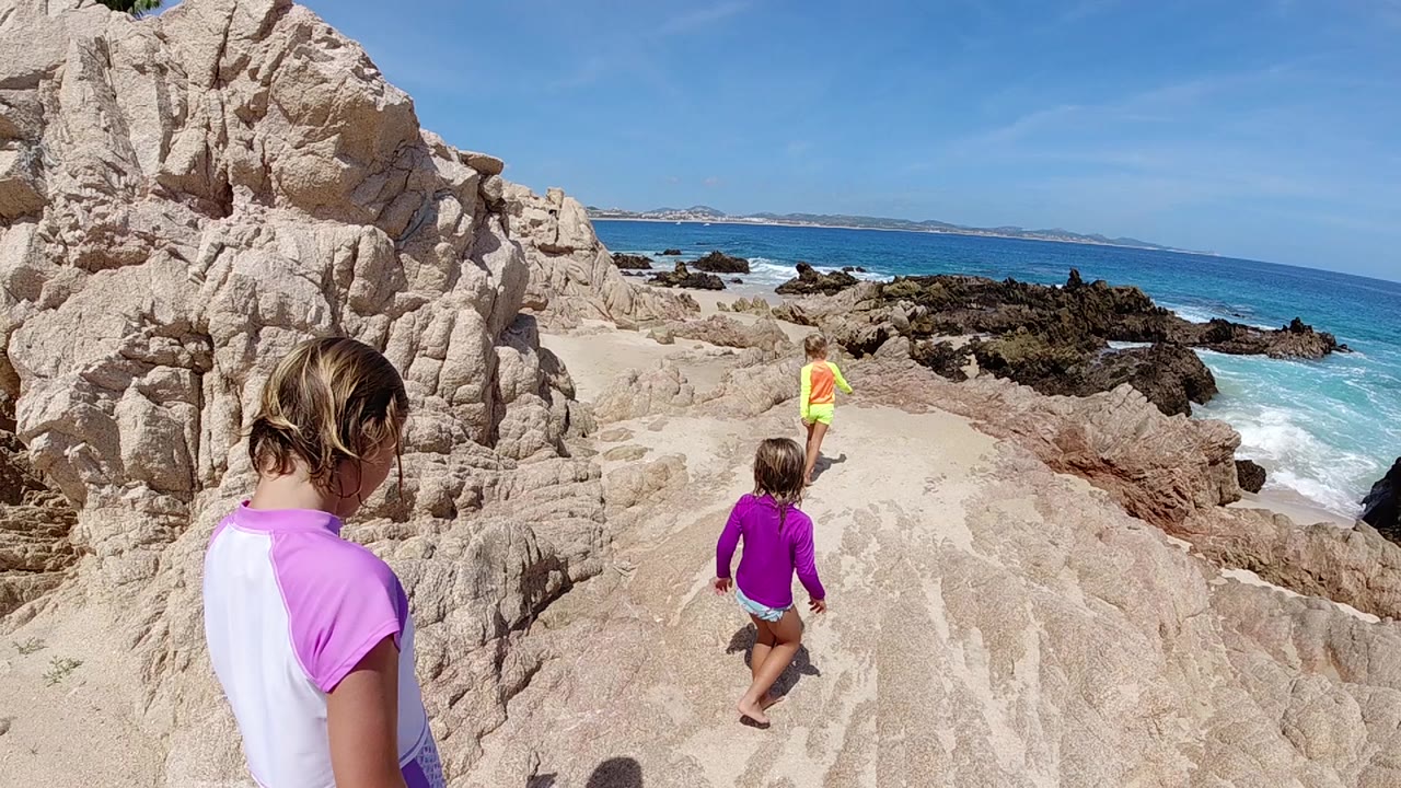 Children running ahead on pale rocks beside surf
