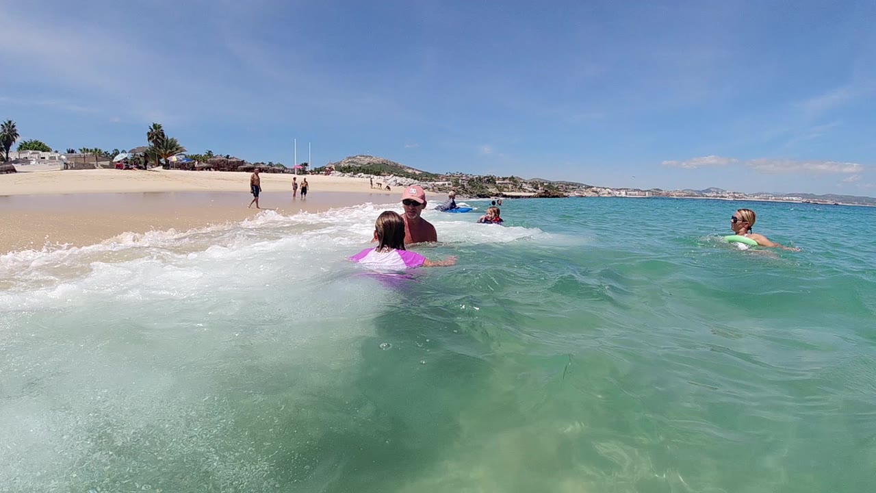 Adult and child wade as a small wave breaks beside them.