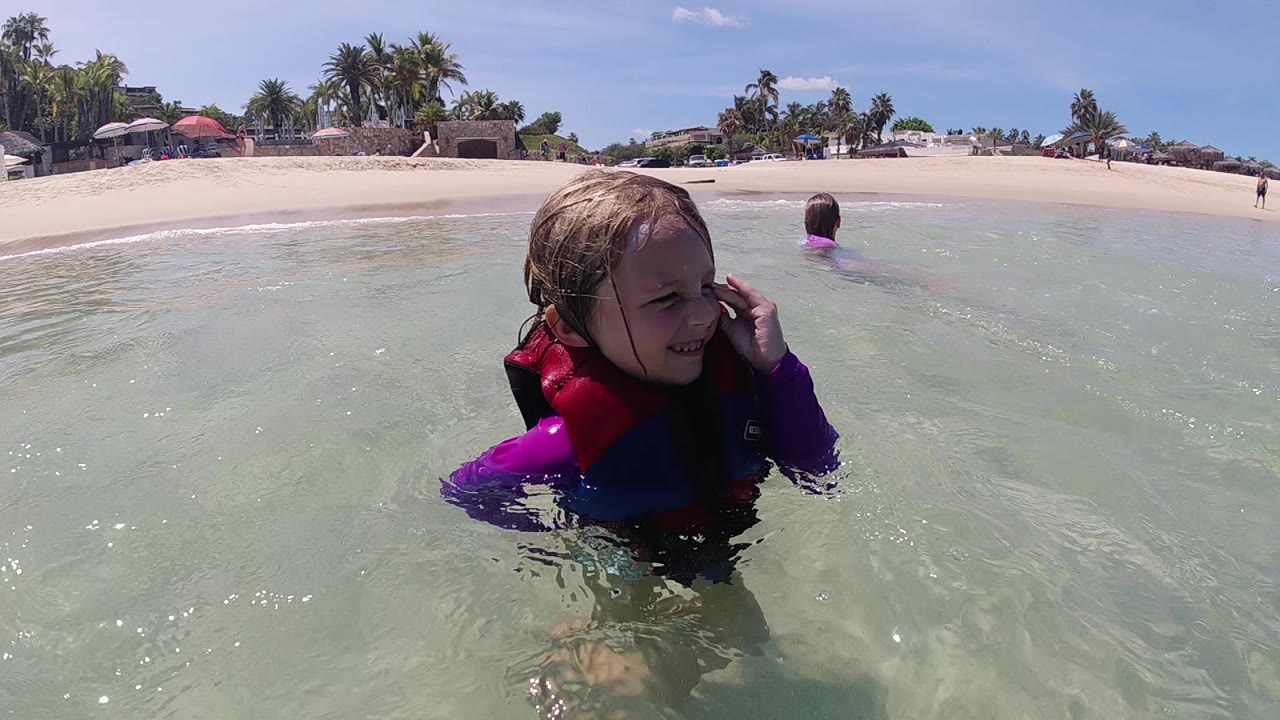 Child in shallow ocean water touching their face.