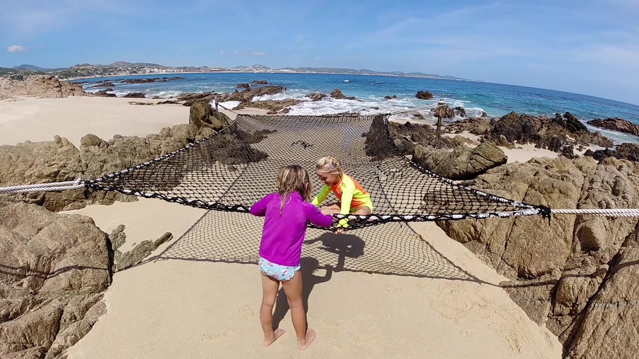 Girl in purple reaches toward a seated child on a rope beach net.