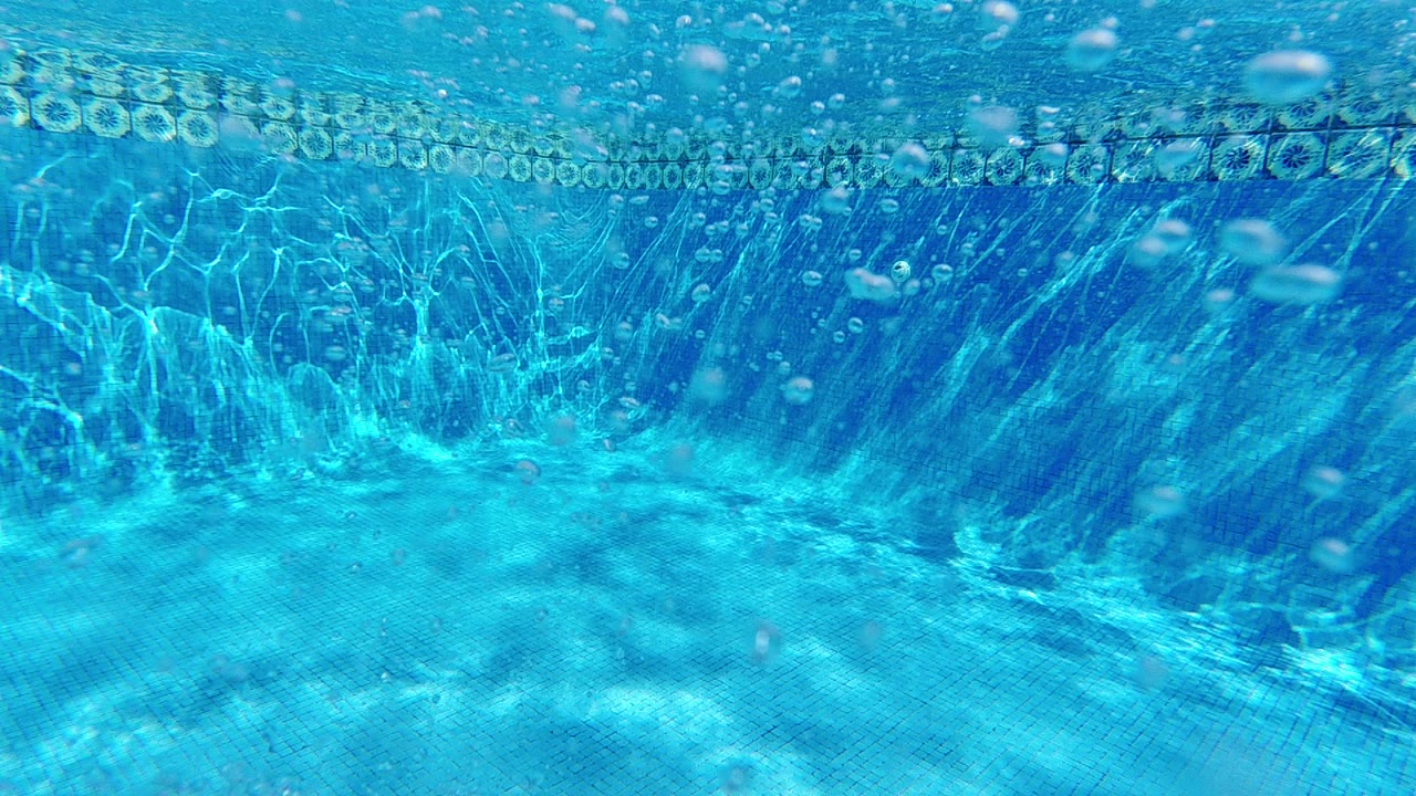 Underwater perspective looking up through clear blue water in Cabo, Baja California Sur, Mexico, with the bright water surface visible in the upper portion and small bubbles rising, no visible people