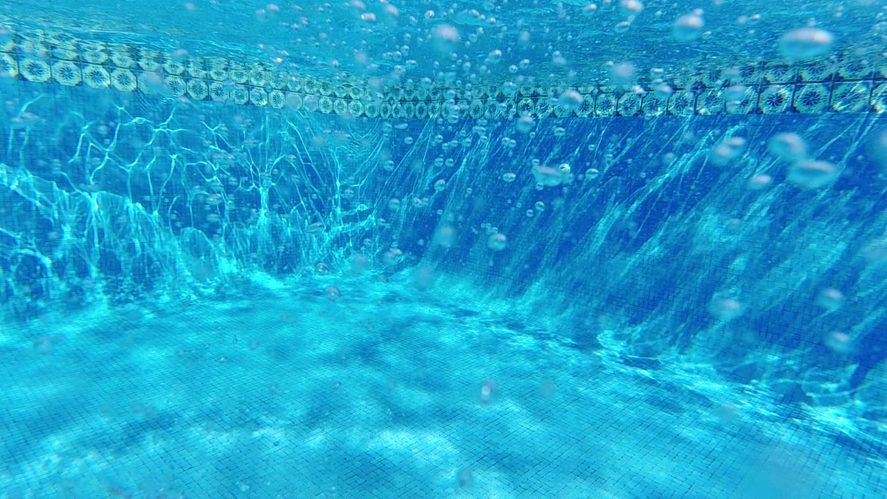 Submerged upward view through clear blue water in Cabo, Baja California Sur, Mexico, showing the bright water surface and caustic light refraction in the upper portion, no visible people