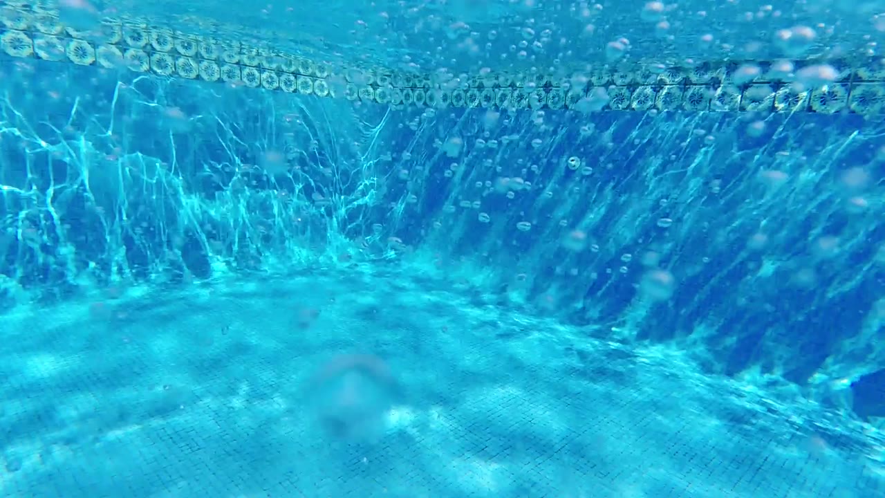Underwater view looking up through clear blue water in Cabo, Baja California Sur, with rippling surface light and small scattered bubbles visible in the upper frame, no visible people
