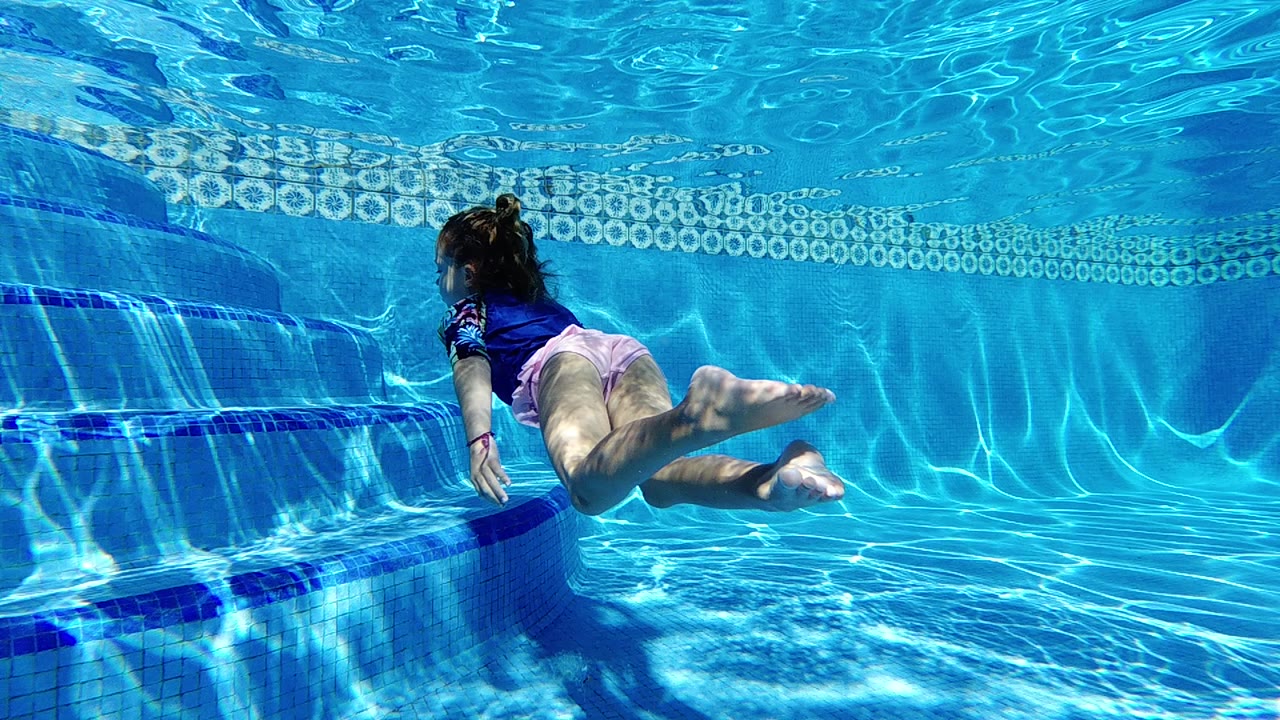 A young girl in a blue swim top and pink bottoms swims underwater near tiled pool steps in Cabo, Baja California Sur.