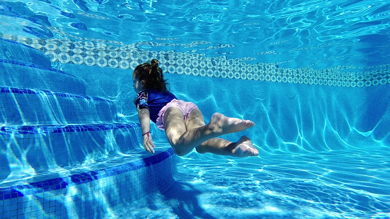 Child swimming underwater with legs extended near pool wall.
