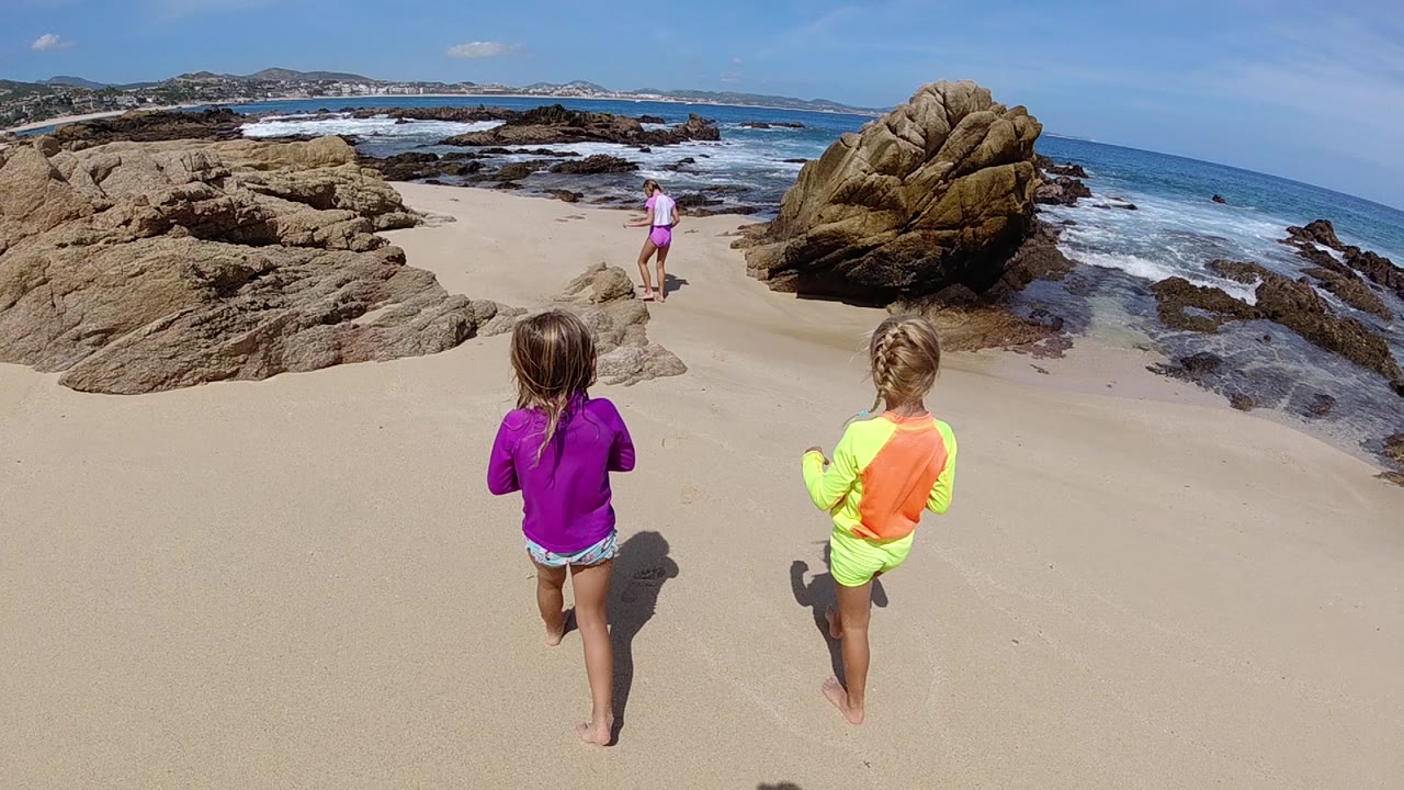 Children continue running along sand between beach rocks.