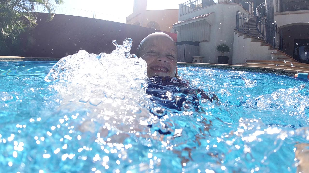 At the start in Cabo, Baja California Sur, a young boy is partly hidden behind a large white splash at water level in a residential pool.