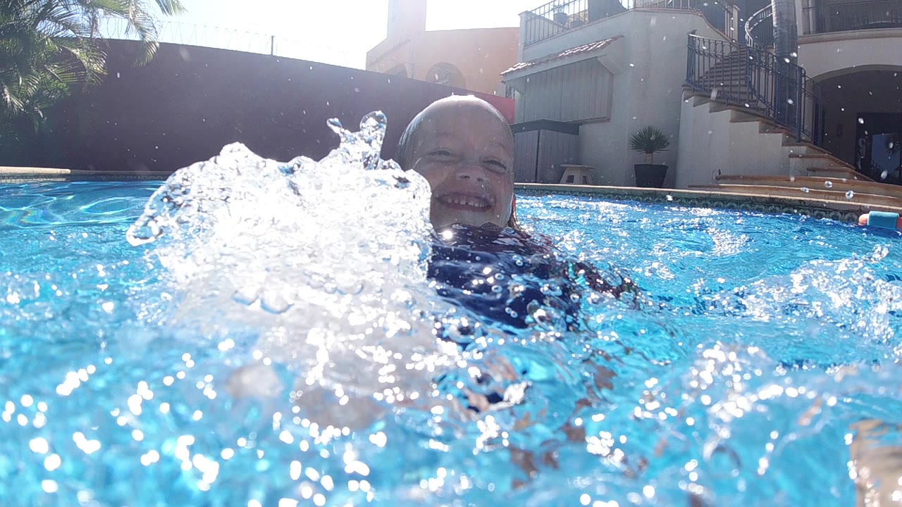 Smiling boy behind splashing blue pool water