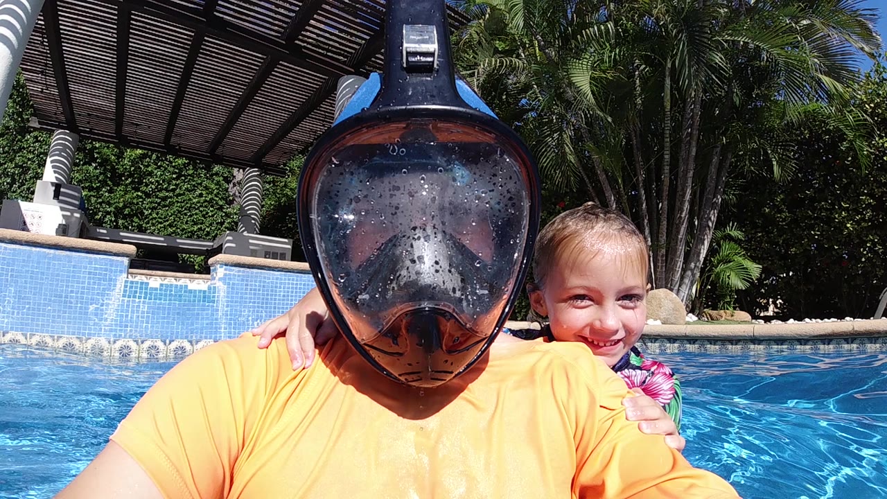 Masked adult centered in the pool with a child smiling over the shoulder.