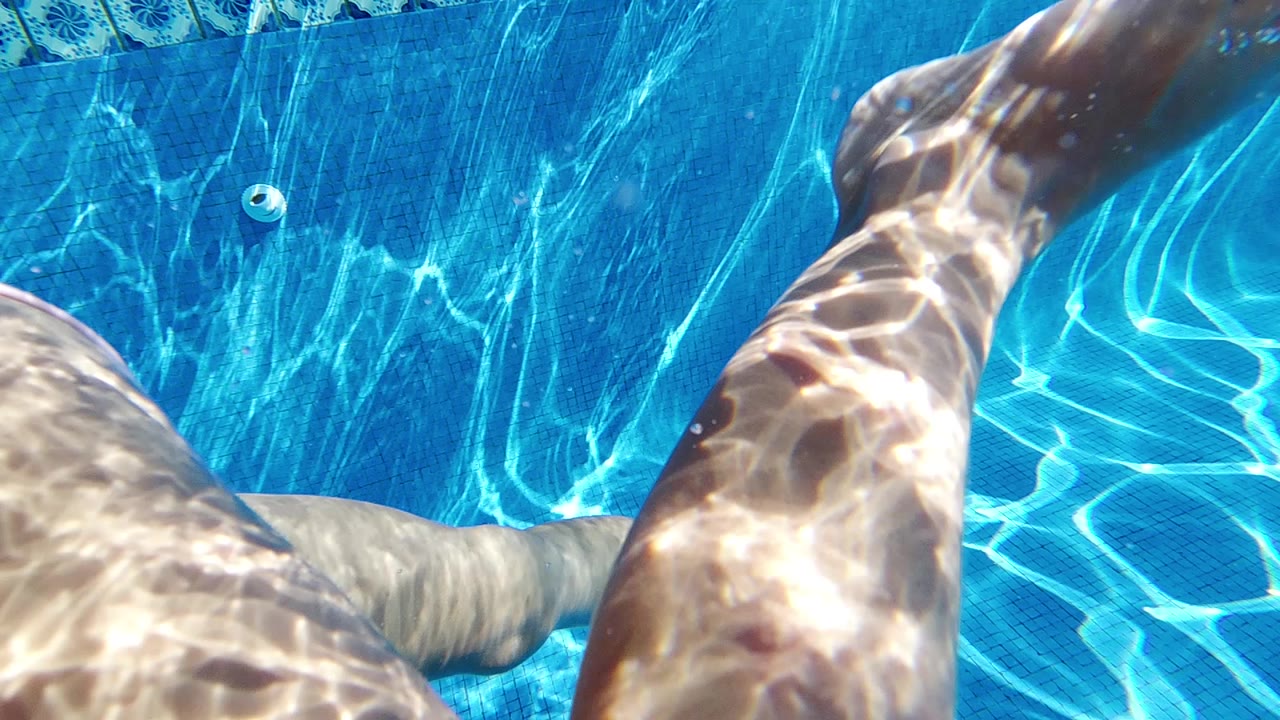 Close underwater view of legs and pool floor