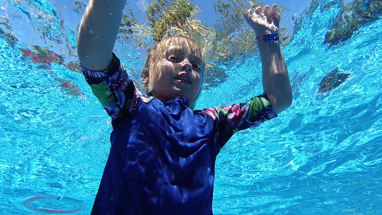 Child underwater with both hands near the rippling pool surface.