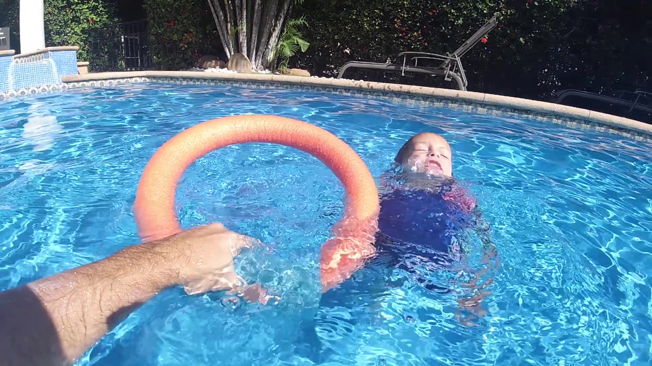 At 0:02, the child has moved to the right side of frame while the orange foam ring remains centered over the rippling Cabo pool water.