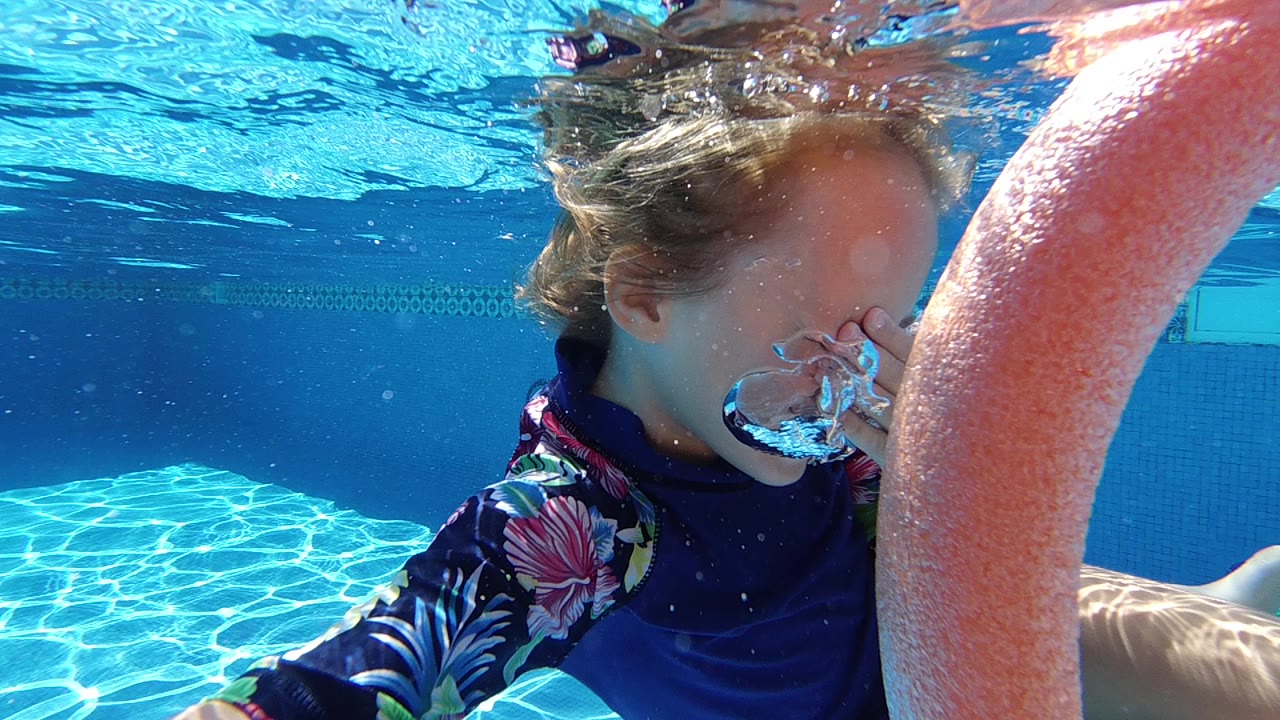 In Cabo, Baja California Sur, a child swims underwater with bubbles at the nose while an orange pool noodle fills the right foreground.