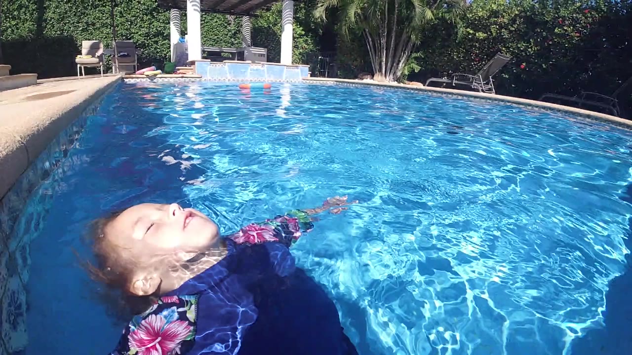 At the start of the Cabo pool clip, a woman floats on her back near the lower left edge while sunlit blue water fills most of the frame.