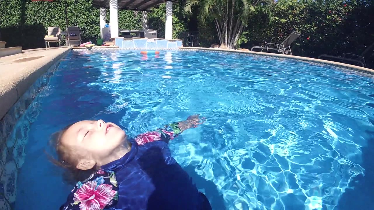 At 0:02, the woman drifts along the lower left while the bright pool opens to the right and white pillars remain visible in the background.