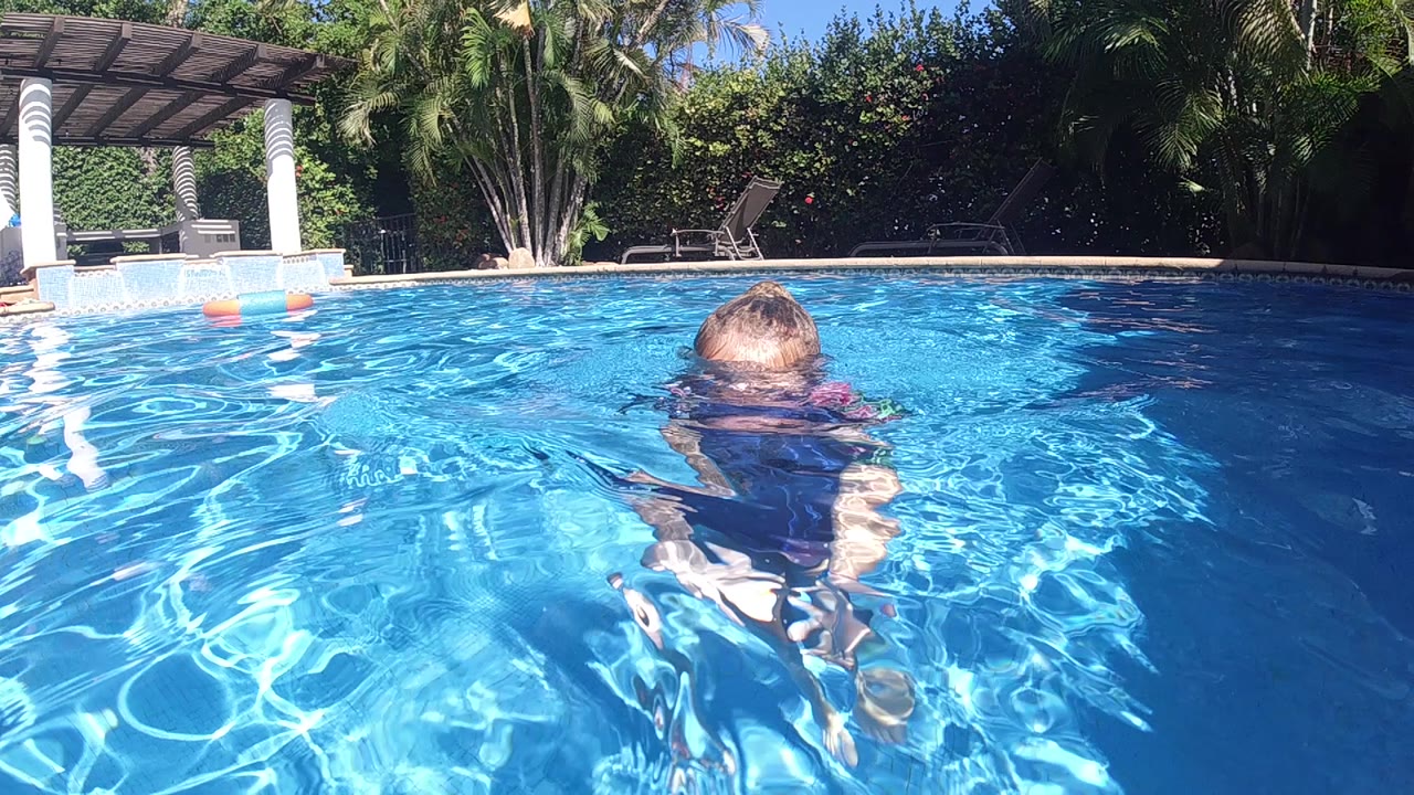Child swimming away from camera in bright pool water.