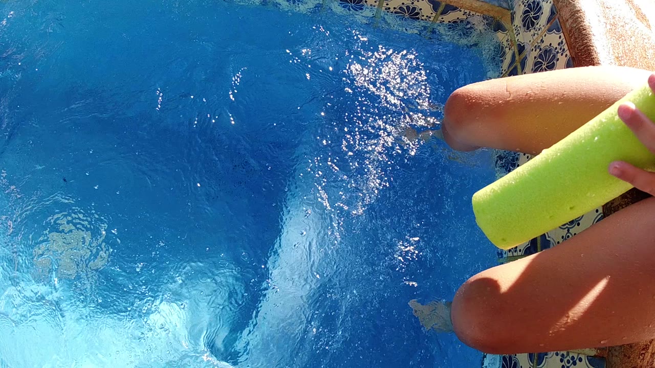 A partial person remains cropped on the right in Cabo, with feet dipping into the blue pool and a lime green cup held close to the water.