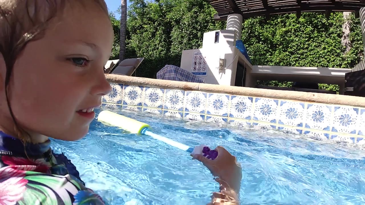 A closer side view shows the girl's wet hair, face, and hand on the foam toy above bright blue water in Cabo, Baja California Sur.