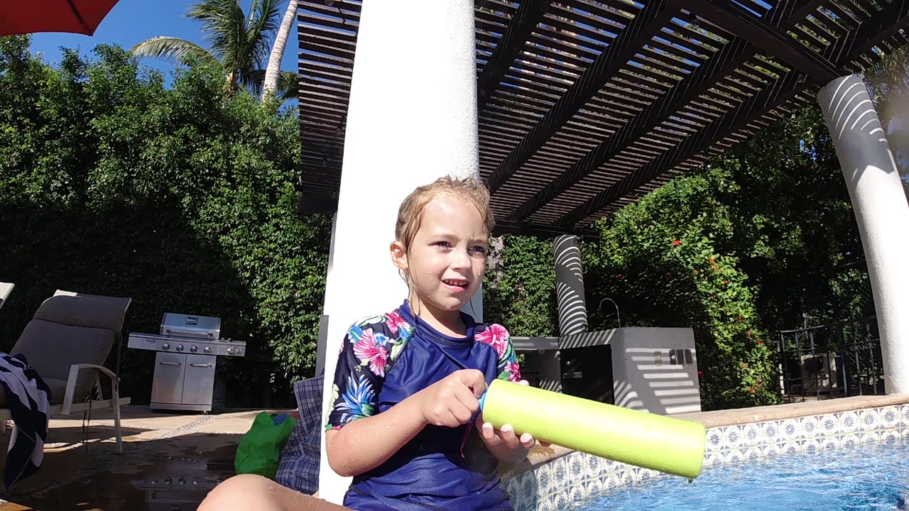 Girl looks ahead while holding a yellow water gun by the pool.