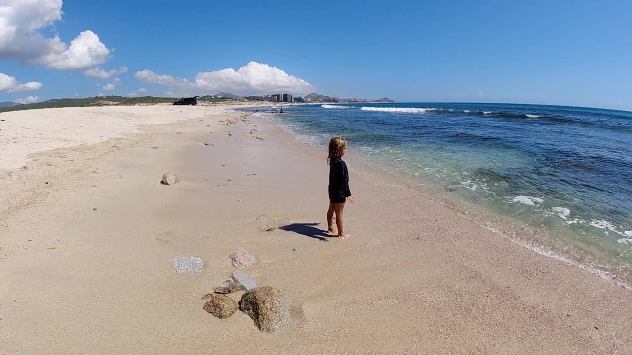Child standing near clear water on a bright sandy beach.