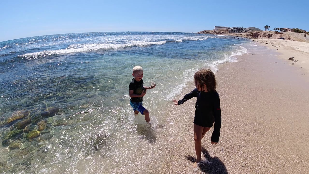 Boy and girl play at the waterline with clear surf behind them.