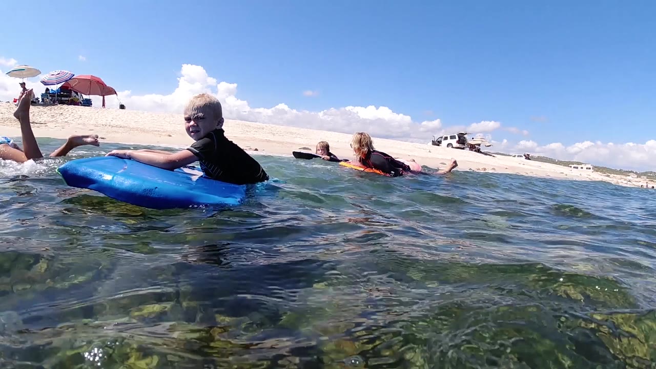 At 0:02 in Cabo, the child on the blue boogie board stays close to frame left while other children on boards appear farther right near the beach.