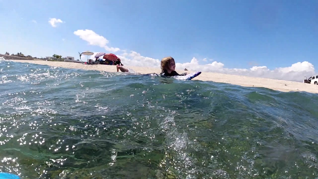 Surfer on board with a low wave between camera and beach.