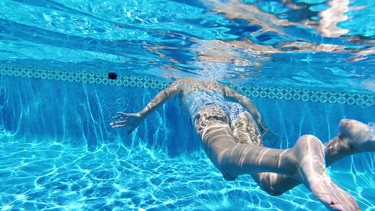 Underwater view in Cabo of a swimmer moving across a bright blue pool, with one bare foot near the lens and tiled pool wall behind.