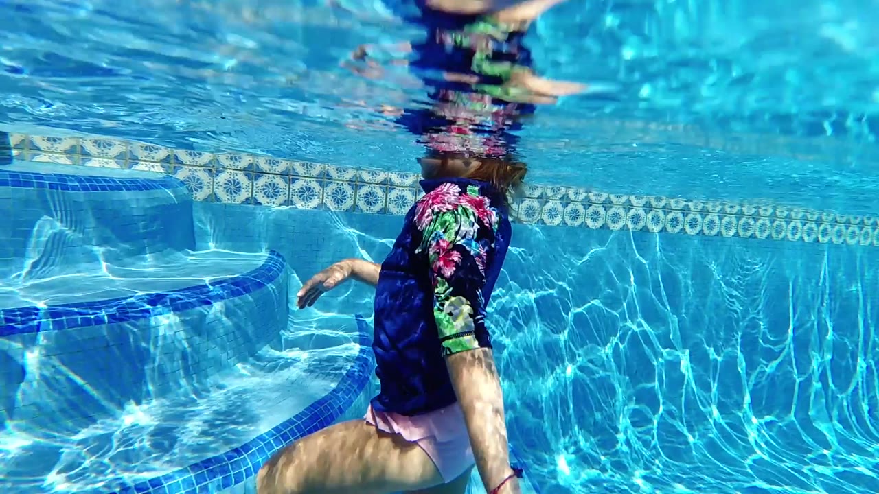 In Cabo, the swimmer has shifted right of the curved pool steps, her torso partly submerged below the wavering surface while sunlight patterns the blue water.