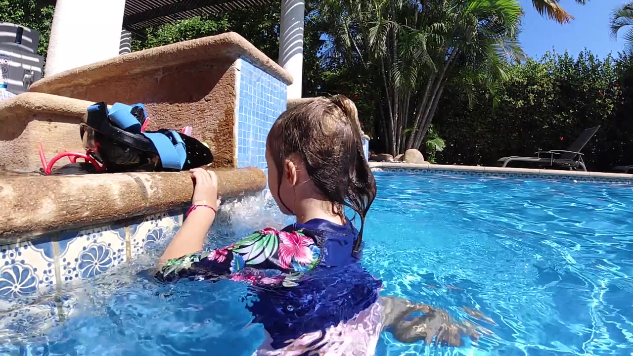 At 0:02 in Cabo, Baja California Sur, the child remains near the ledge as sunlight makes sharp ripples across the blue pool and the tiled wall fills the left side.