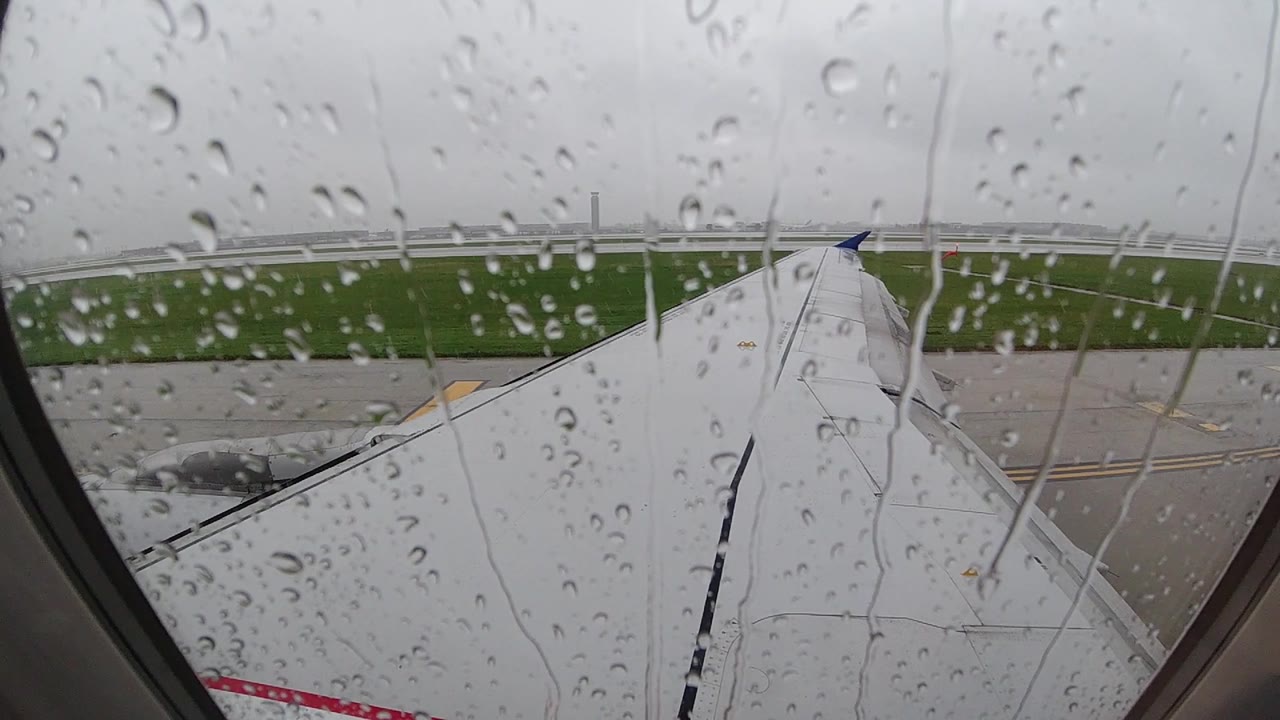 Water droplets scattered across a passenger airplane window at a Chicago-area airport in 2019, with the white aircraft wing and grey tarmac visible beyond; no people visible