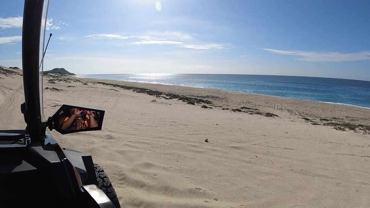 POV drive on beach, roll cage left, orange safety flag, ocean visible right, sand foreground