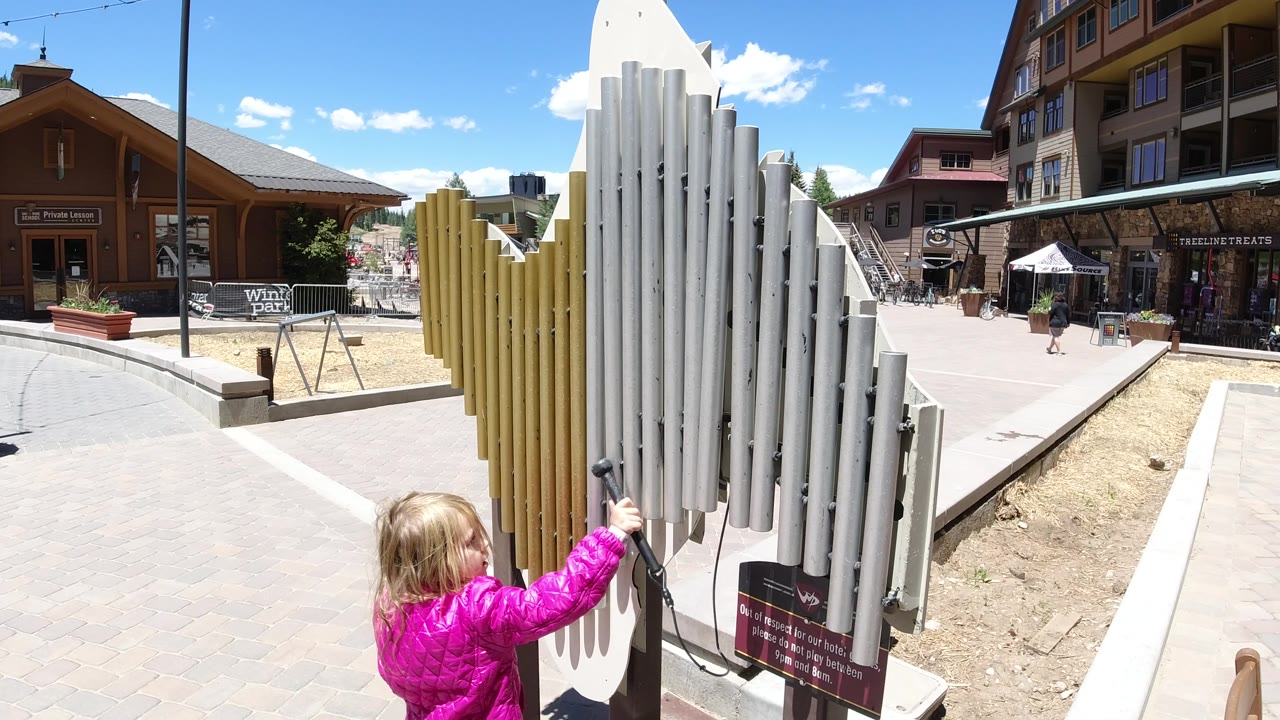 Child stands closer to the white pipes in a sunny square.