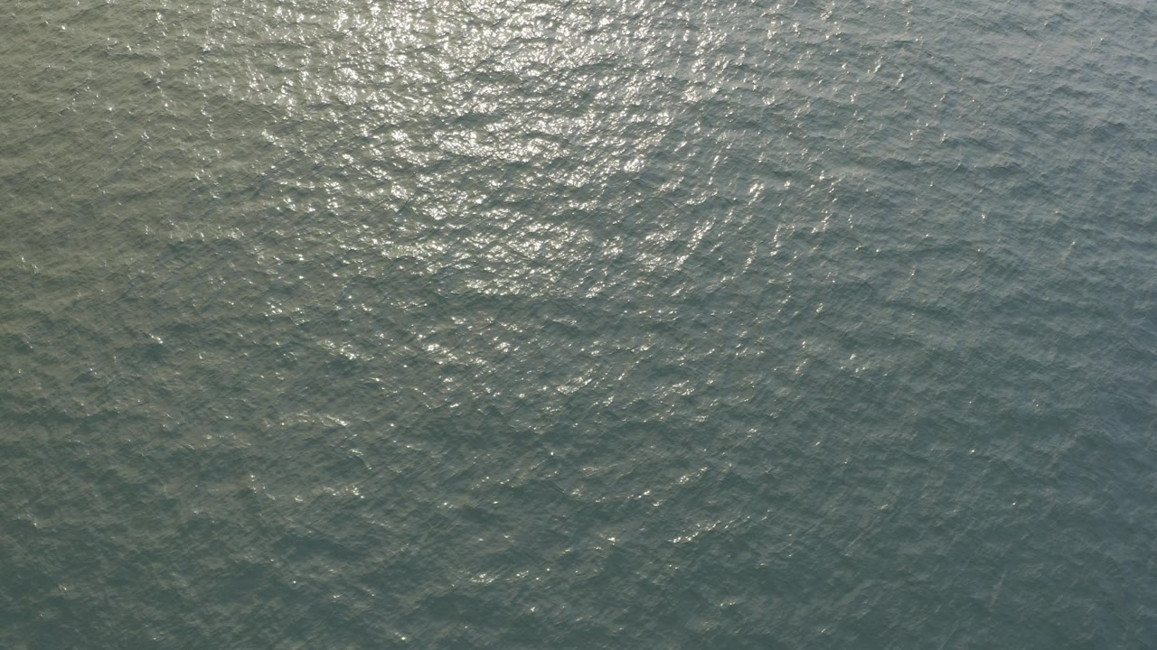 Top-down ocean surface with bright sunlight shimmer.