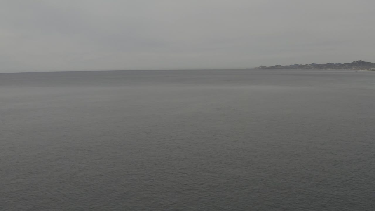 Wide grey ocean under an overcast sky with distant land on the horizon