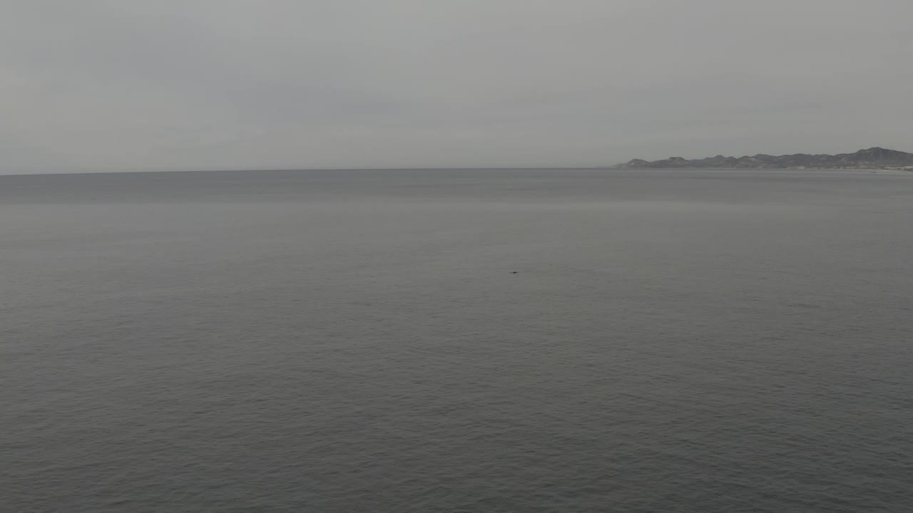 Wide aerial-feeling seascape with smooth grey water, a level horizon, distant low land, and no visible people.