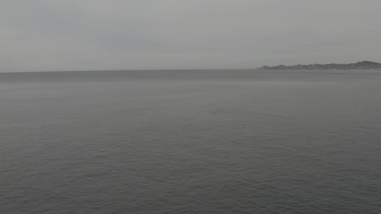 Calm grey sea under an overcast sky with a distant landmass on the right