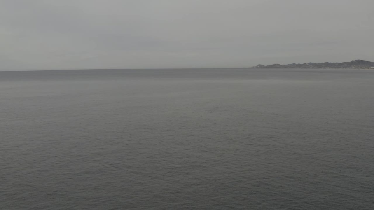 Wide view of smooth grey water stretching to a level horizon, with the distant landmass sitting slightly right of center and no visible people.