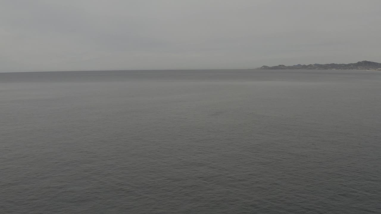 Grey water fills most of the frame below a soft cloudy sky, while a faint coastline remains on the upper right with no boats or visible people.