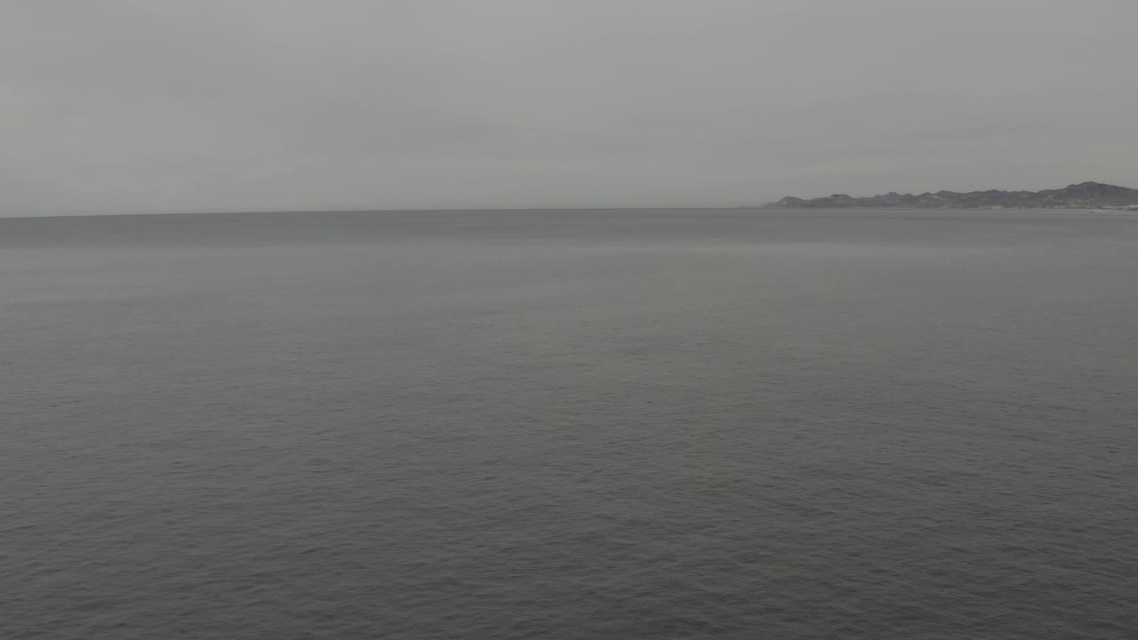 Calm rippled water leads toward a pale grey horizon, with the distant landmass more centered across the upper frame and no visible people.
