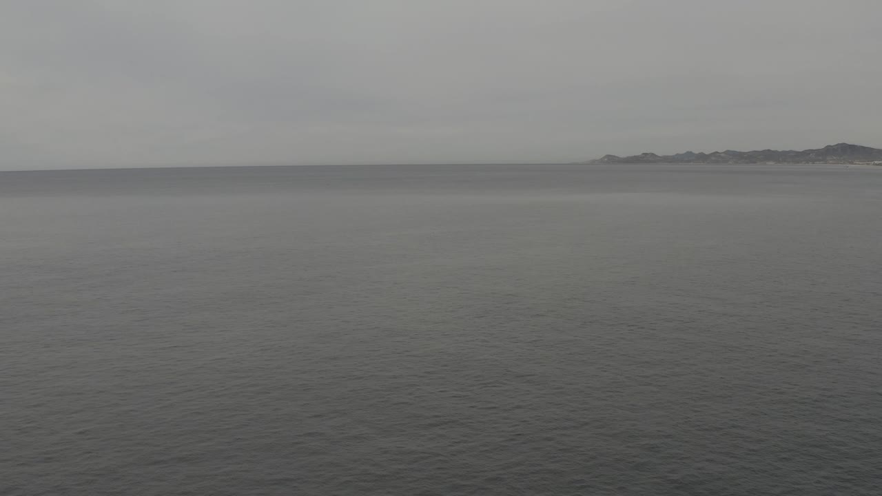 A broad field of rippled grey water fills most of the frame while the pale sky and low distant land remain soft in haze, with no visible people.