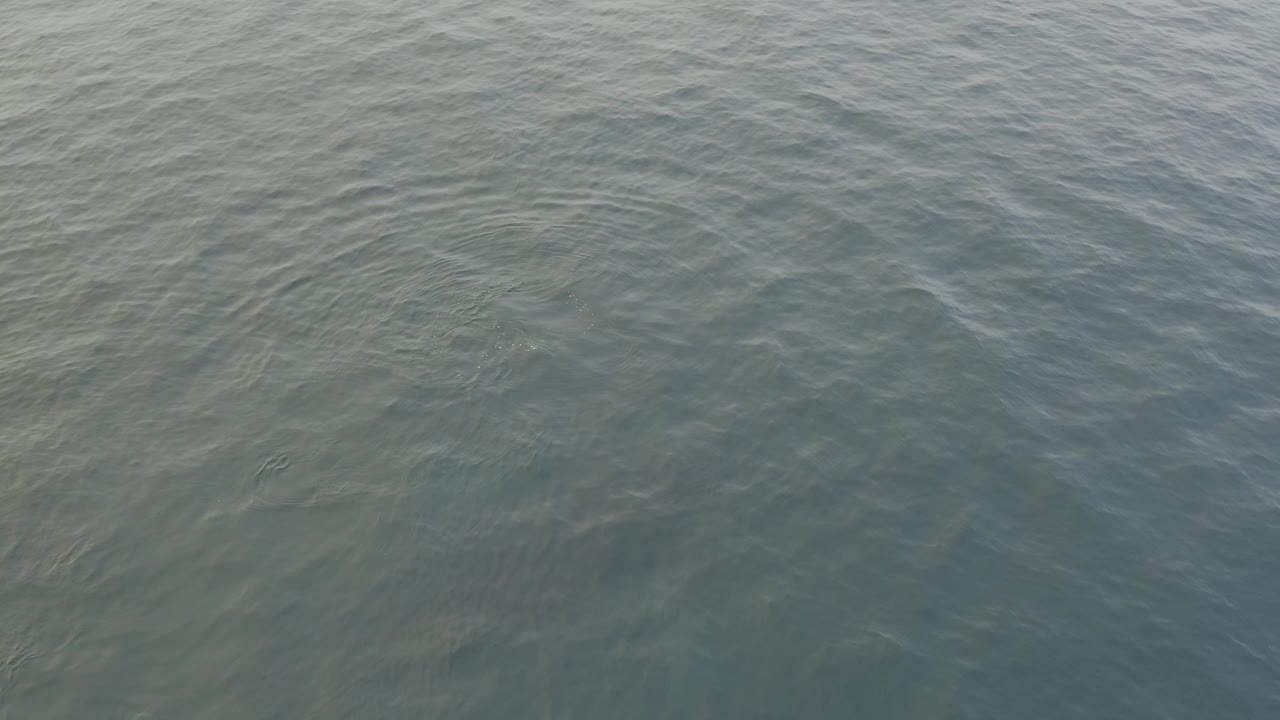 The third frame keeps the view tight on open grey water, where soft wave lines create a lightly mottled surface and no visible people appear.