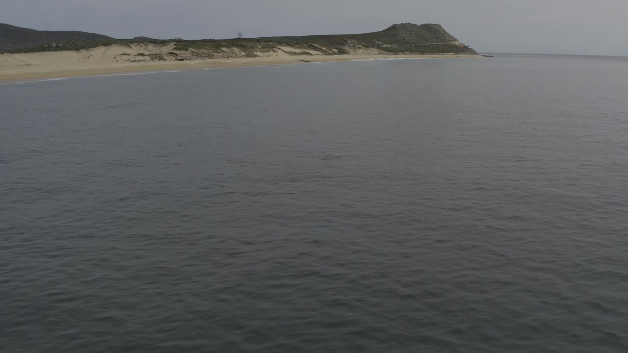 Aerial view of calm grey-blue sea facing a sandy coast and low dunes.