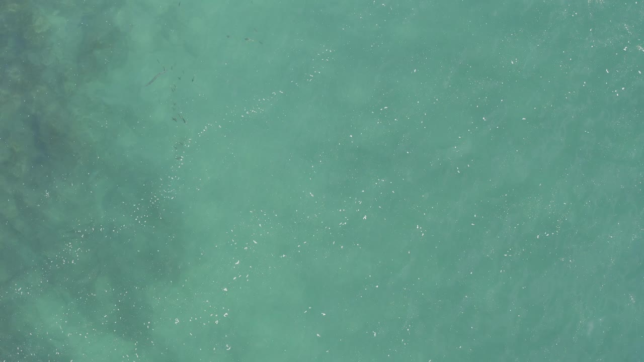 Top-down turquoise ocean surface with darker underwater patches