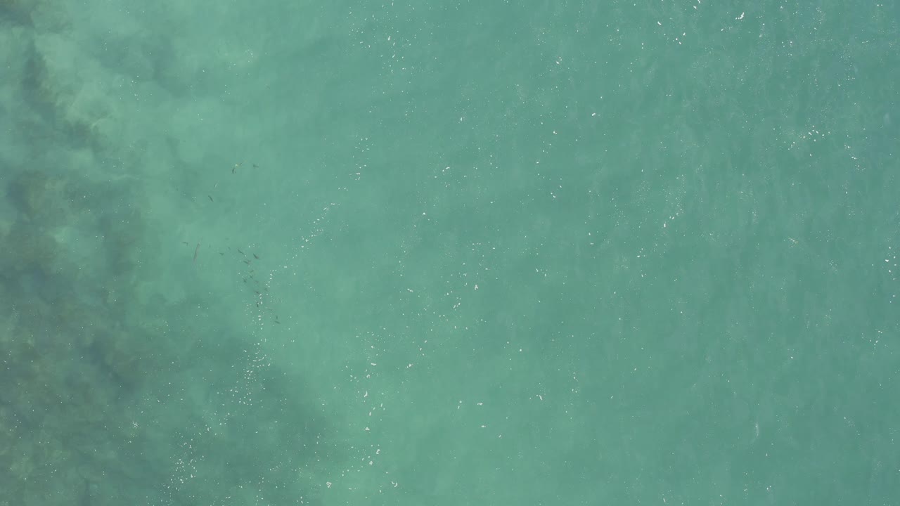 Top-down turquoise ocean surface with darker cloudy streaks.