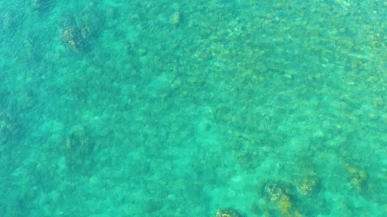 Turquoise ocean water at Playa Acapulquito in Los Cabos covers scattered submerged rocks, with soft ripples crossing the frame and no visible people.