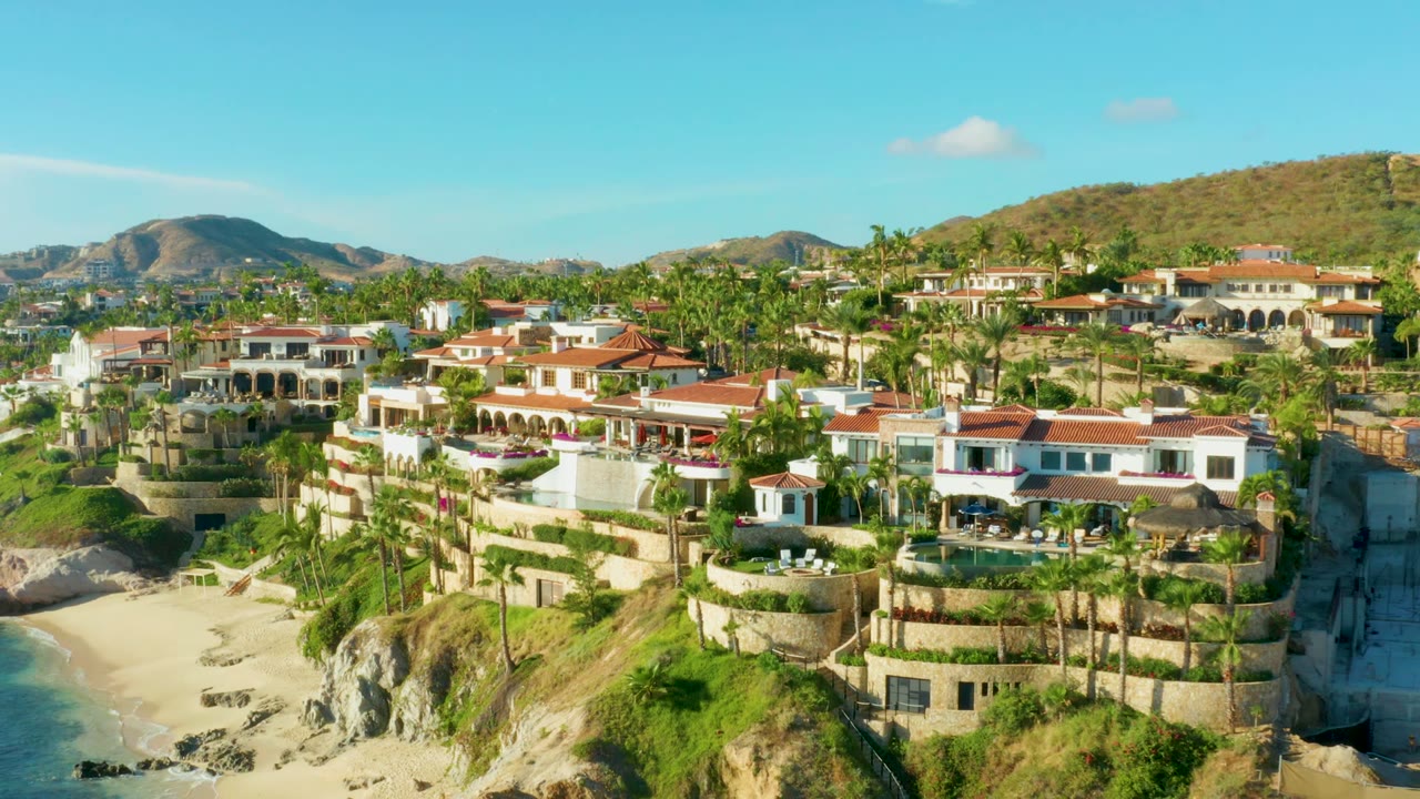 Hillside residential complex with palms, beach, and mountains behind.